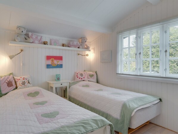Ein gemütliches Schlafzimmer mit zwei Betten, einem Regal mit Dekoration, einem Gemälde und einem Fenster mit Jalousien.
