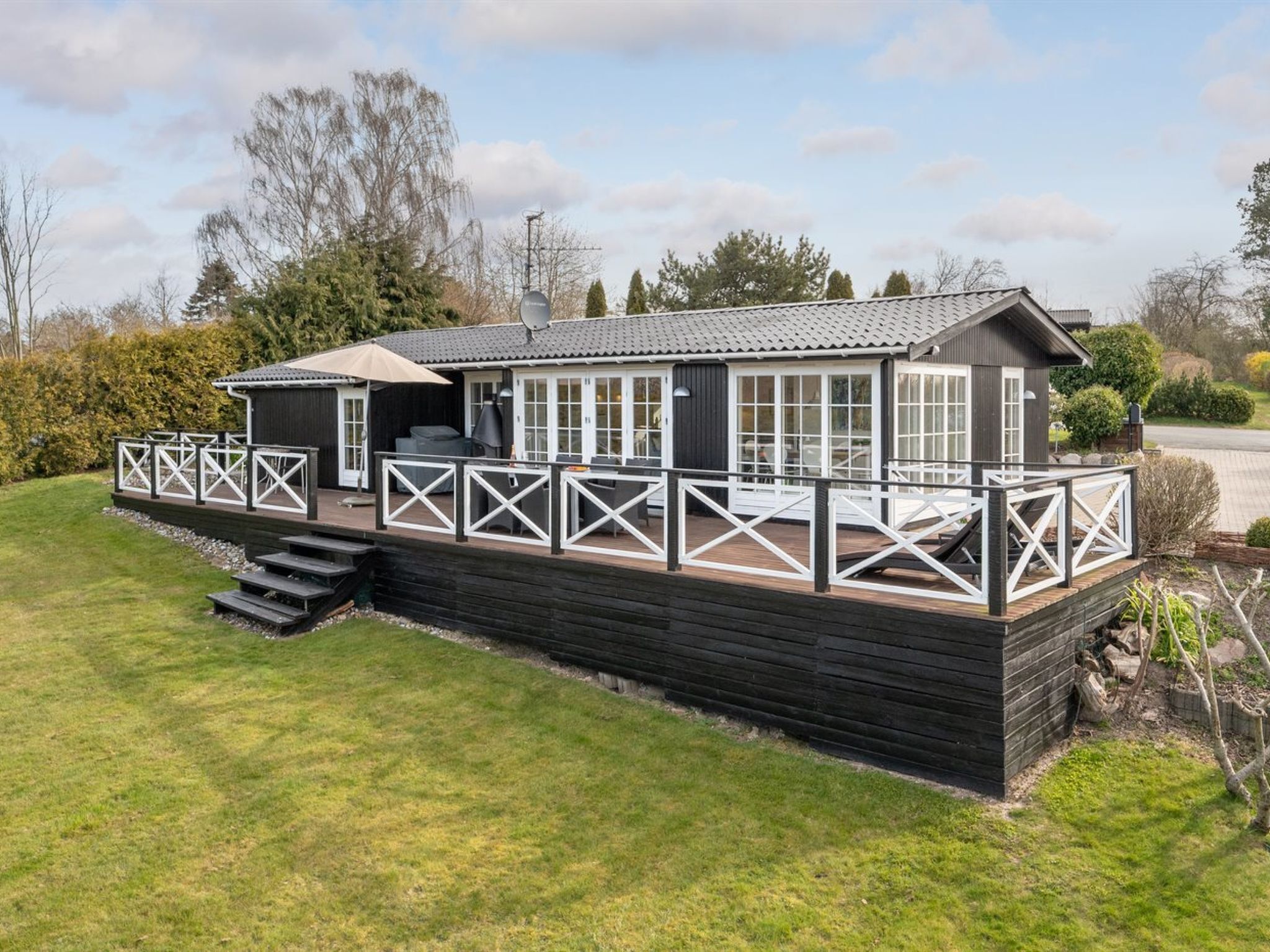 Ein zweistöckiges Holzhaus mit einer Terrasse und einem überdachten Außenbereich zum Sitzen.