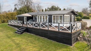 Ein zweistöckiges Holzhaus mit einer Terrasse und einem überdachten Außenbereich zum Sitzen.