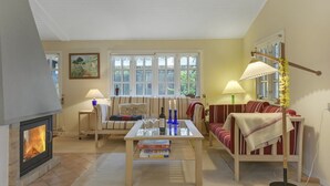 Un salon chaleureux avec une cheminée, un canapé, une table basse avec des livres et une fenêtre avec des rideaux.