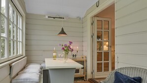 Une pièce chaleureuse avec un banc, une table sur laquelle se trouvent une bouteille et des verres, et une chaise avec un coussin.