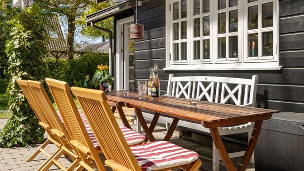 Une terrasse extérieure avec une table et des chaises en bois, un banc blanc et une fenêtre à carreaux.