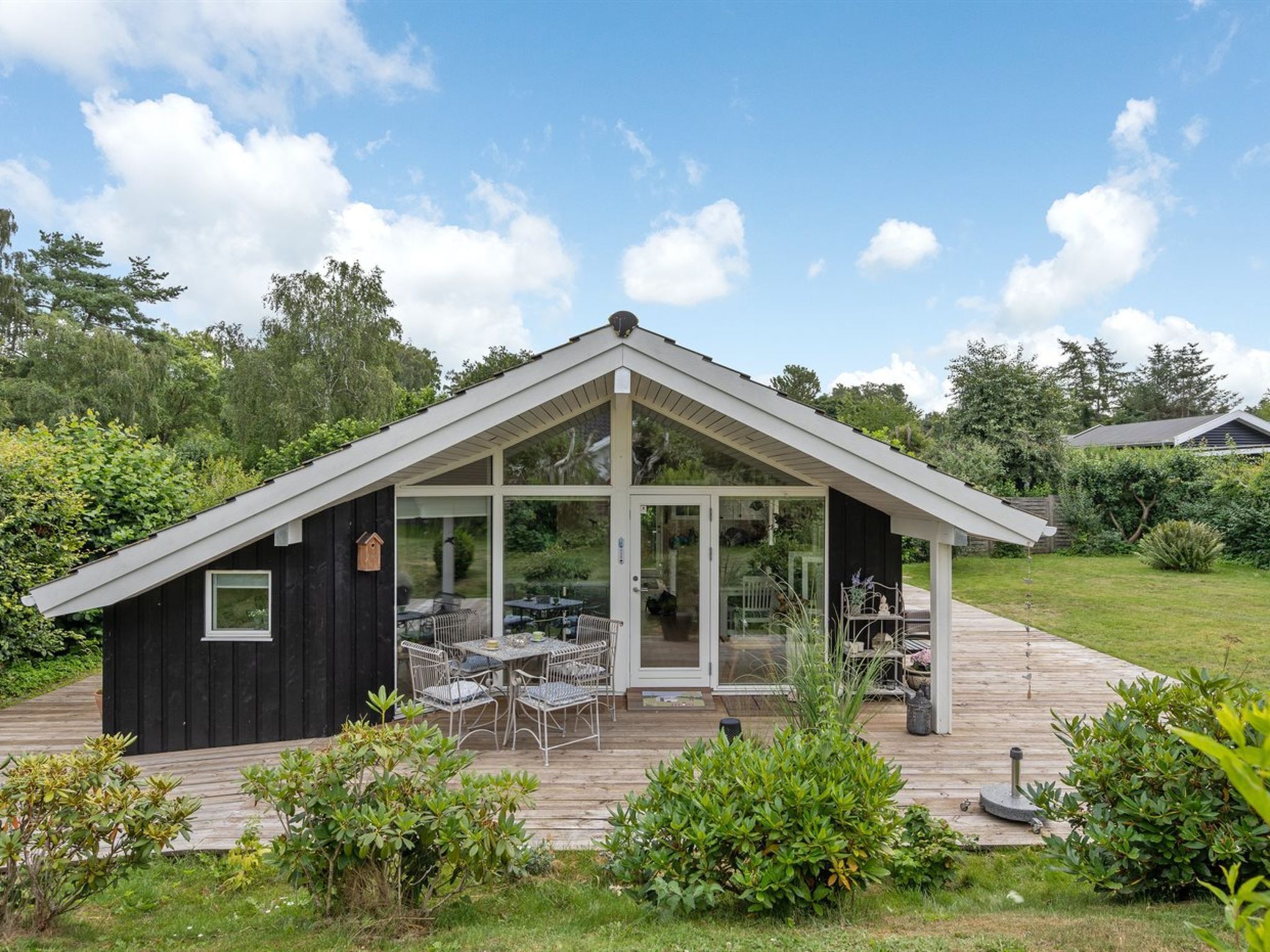 Ein modernes Haus mit Wintergarten, einer Terrasse und Gartenmöbeln sowie einem Holzboden.