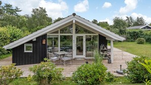 A modern house with a glass conservatory, a patio with outdoor furniture, and a wooden deck.
