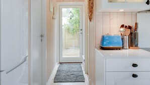 A narrow hallway with a white door, a small rug, and a kitchen area with a blue appliance and utensils.