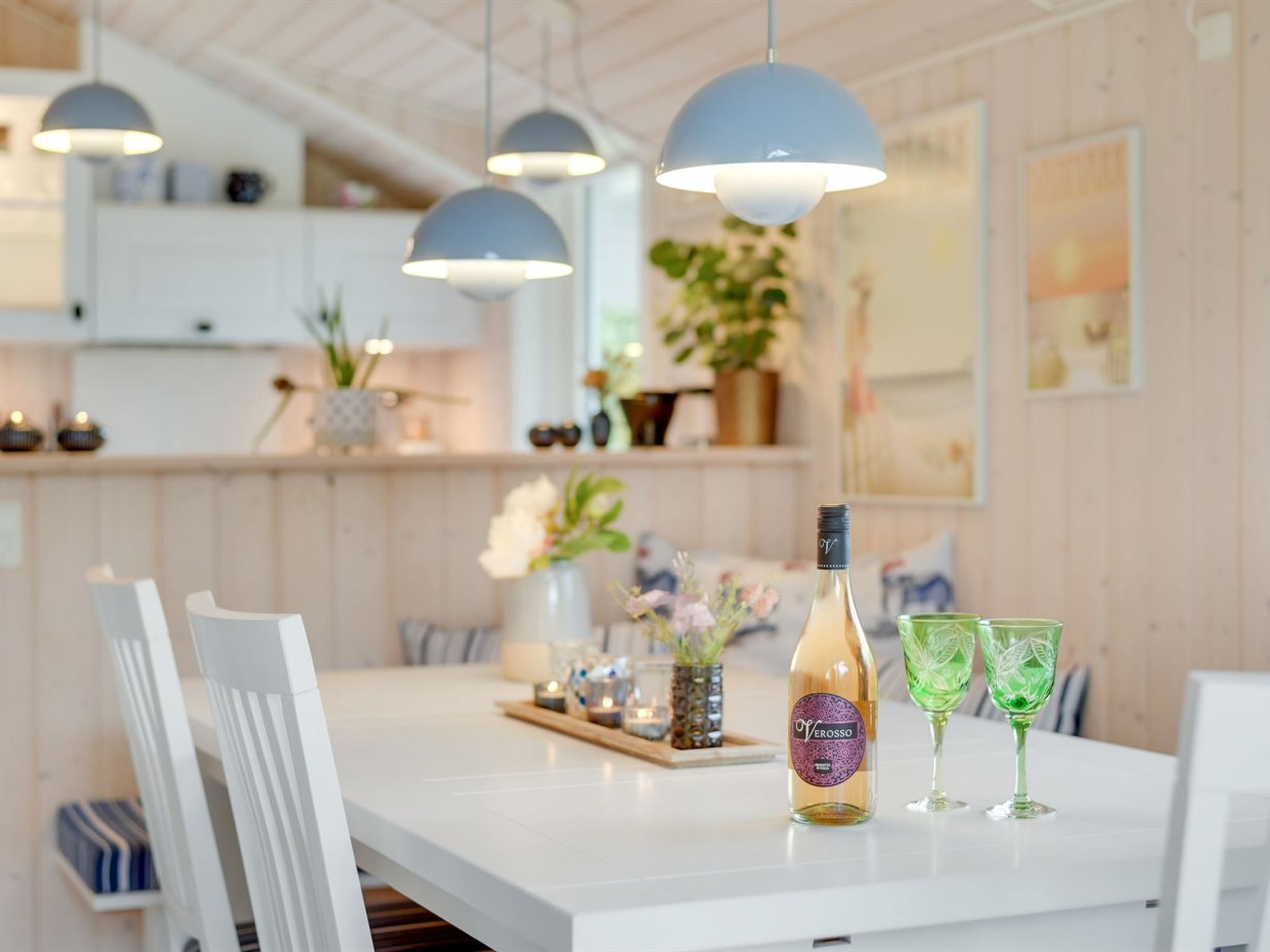 A modern kitchen with white cabinetry, pendant lighting, and a dining table set with a bottle and glasses.