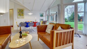 Un salón amplio con un ventanal grande, un comedor con sillas coloridas y una zona de estar acogedora con un sofá de cuero.