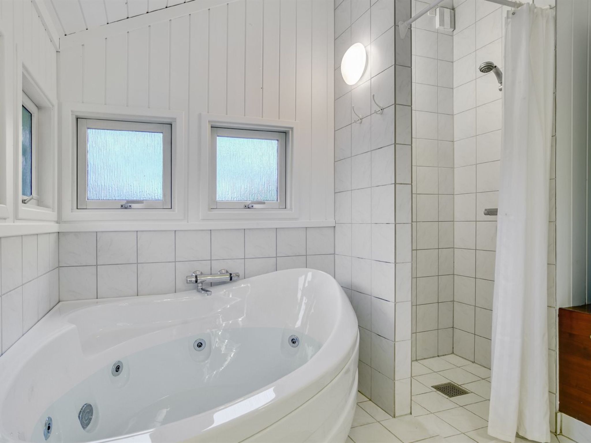A modern bathroom with a large bathtub, a shower area, and two windows providing natural light.