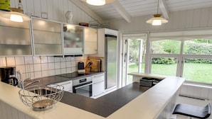 Une cuisine moderne avec des meubles blancs, un îlot central doté de tabourets de bar et une vue sur le jardin grâce à de grandes fenêtres.