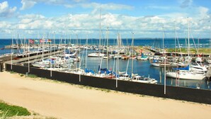 Un port de plaisance où de nombreux bateaux sont amarrés le long d’une plage de sable, sous un ciel dégagé.