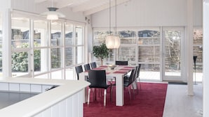 Un coin repas avec une table dressée pour six personnes, entourée de chaises, d’un tapis rouge et d’un luminaire suspendu.