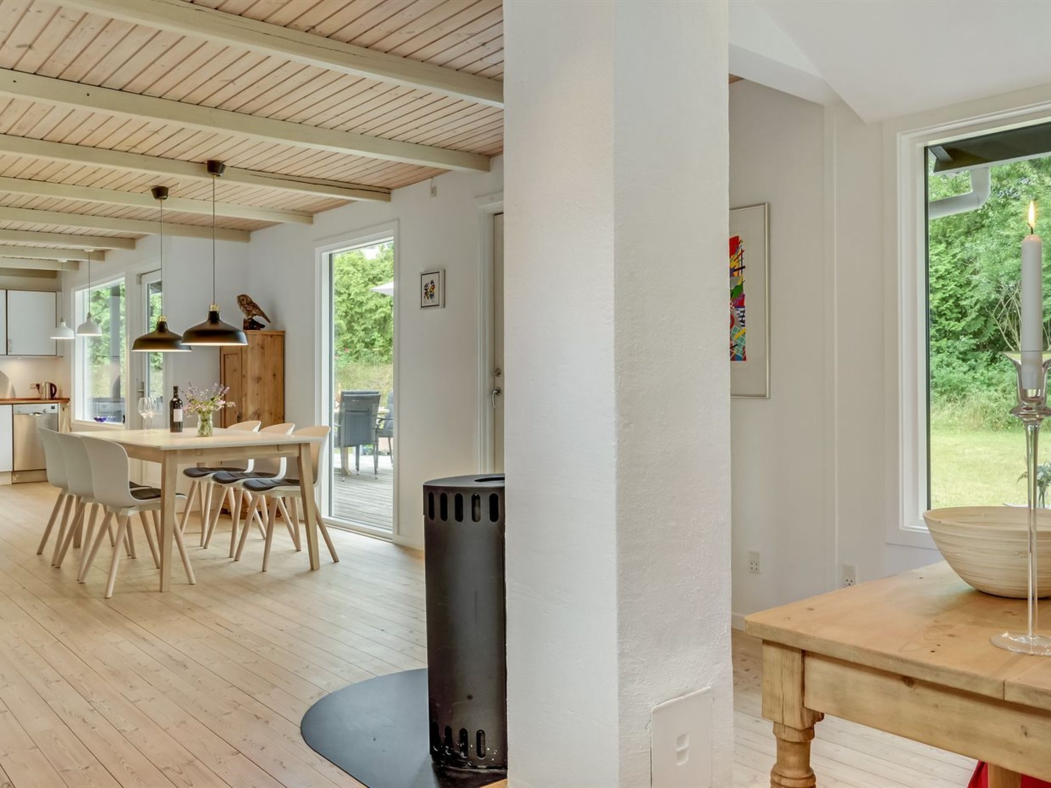 A spacious kitchen with wooden flooring, a dining area with a table and chairs, and a large window with a view of greenery.