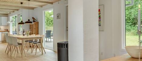 A spacious kitchen with wooden flooring, a dining area with a table and chairs, and a large window with a view of greenery.