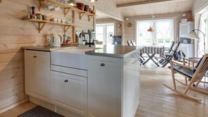 Una cocina moderna con armarios blancos, estantes de madera y un comedor con sillas a rayas.