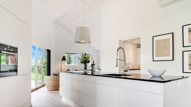 A modern kitchen with a large island, white cabinetry, and a black countertop.
