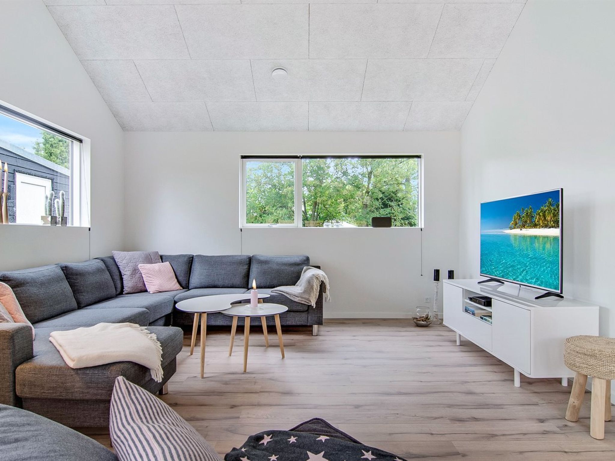 Una sala moderna con un sofá seccional gris, una mesita redonda pequeña, un televisor de pantalla plana y un mueble blanco.