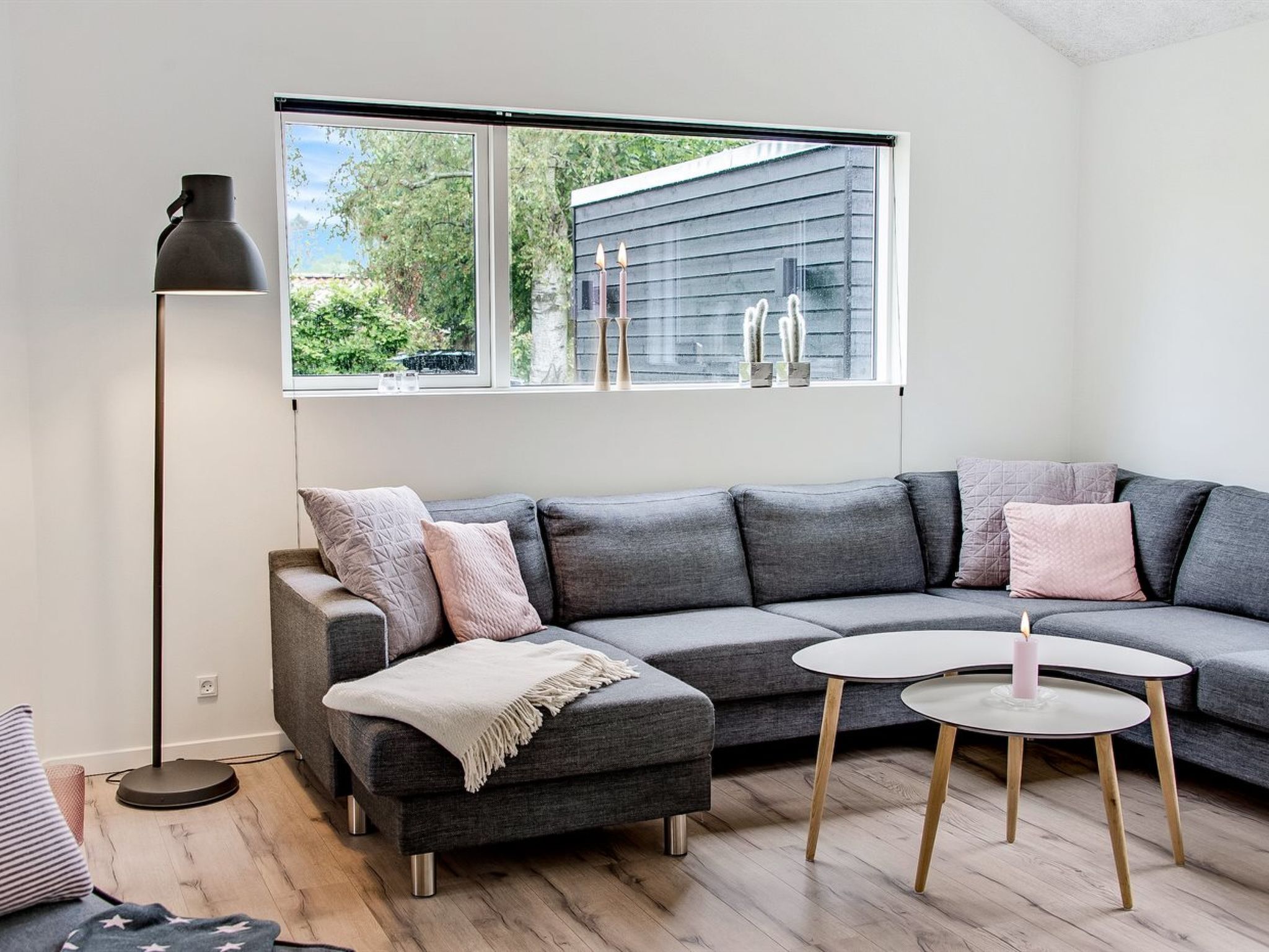 A modern living room with a grey sectional sofa, a small round table with a candle, and a floor lamp.