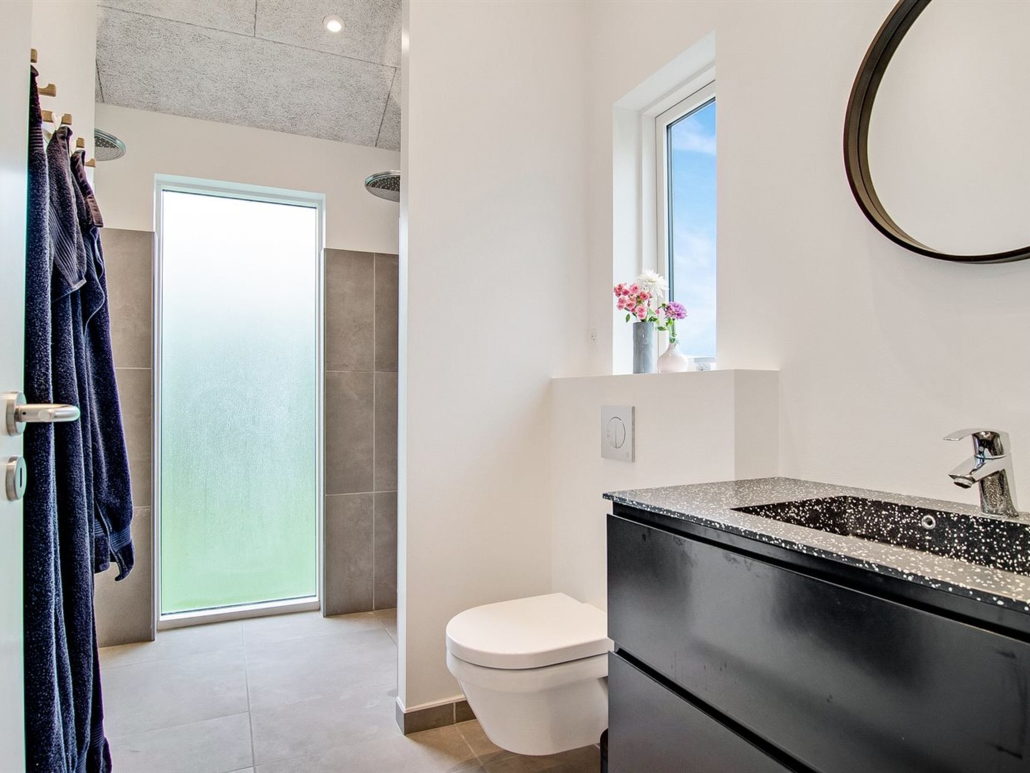 Une salle de bain moderne dotée d’une grande fenêtre, de toilettes et d’un lavabo noir avec un plan de toilette à motifs.