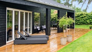 A modern house with a wooden deck, outdoor seating, and a large sliding glass door.
