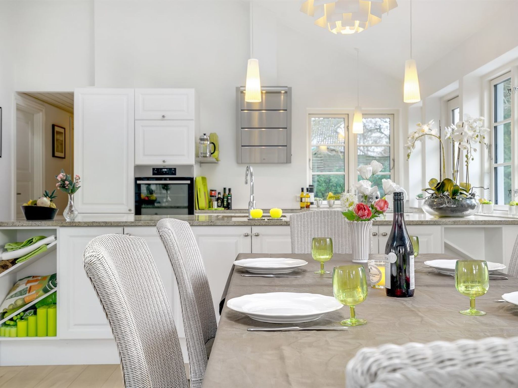 Une cuisine moderne avec des armoires blanches, un four encastré et un coin repas avec une table dressée pour quatre personnes.