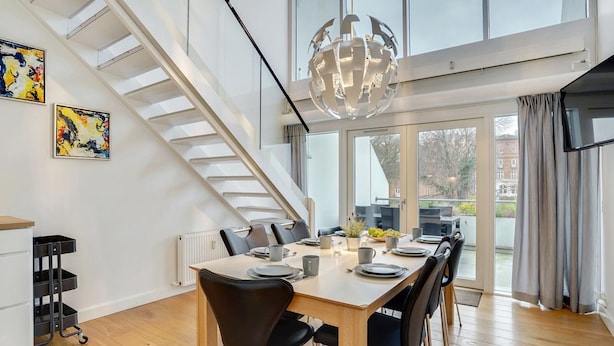 A modern dining area with a wooden table, black chairs, and a large chandelier. A staircase with glass railings leads to an outdoor balcony. - "Pekka" - 50m from the sea by Interhome (Helsingør)