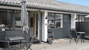 Moderni rakennus, jonka ulkoseinät ovat harmaat, siinä on suuret ikkunat ja ulkotila, jossa on patio ja ulkokalusteita.