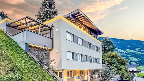 Ein modernes Mehrstöckiges Hotel mit Glasfassade, einer Treppe, die zum Eingang führt, und Blick auf die umliegende Landschaft.