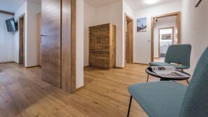 Ein modernes Hotelzimmer mit Holzböden, einem großen Kleiderschrank, einer Sitzecke mit Tisch und einem an der Wand befestigten Fernseher.