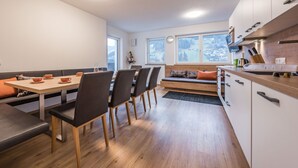 Eine moderne Küche mit Holzschränken, eine Essecke mit einer Bank und große Fenster mit Blick ins Freie.