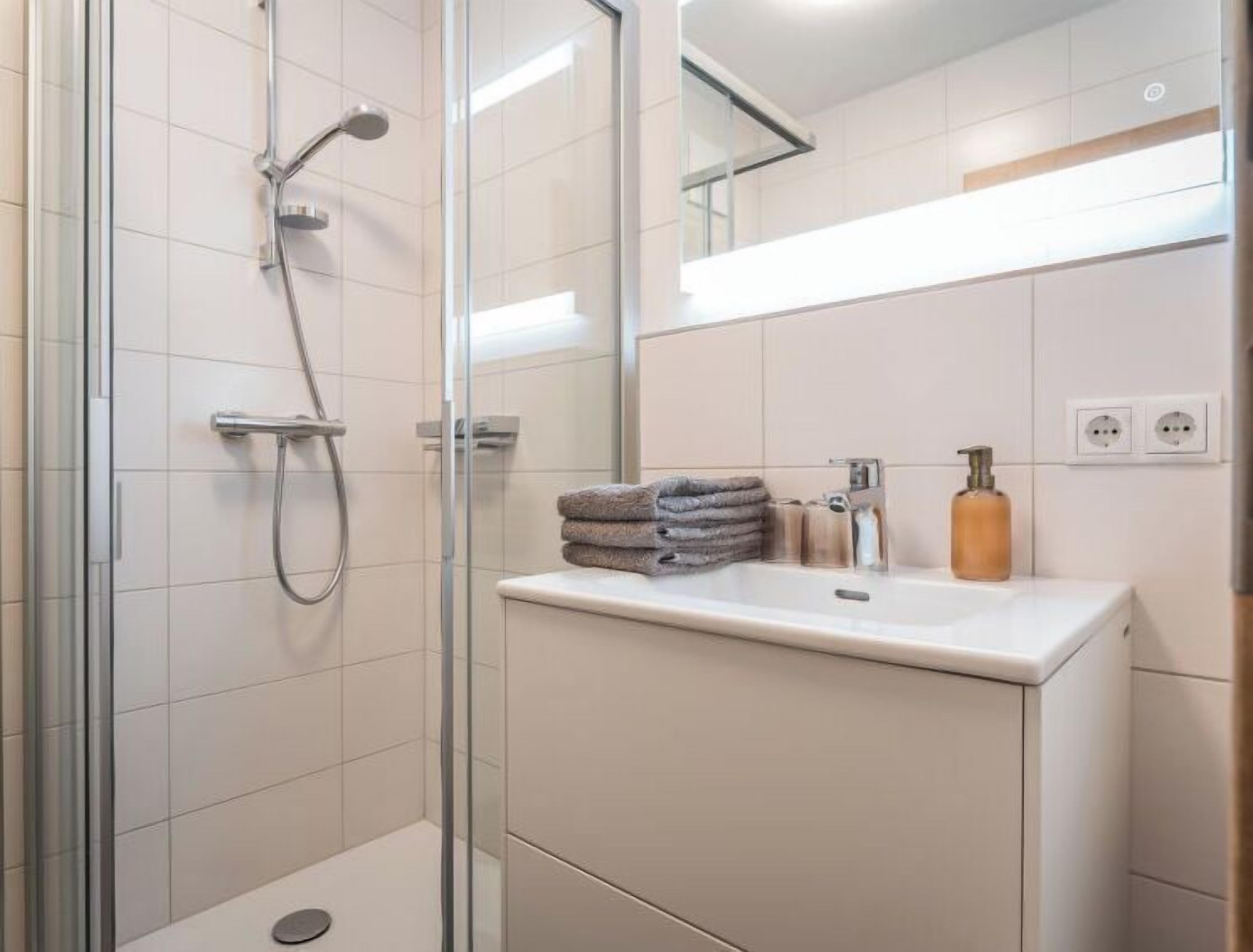 A modern bathroom with a glass shower enclosure, a white sink with a mirror above, and a towel rack with folded towels.