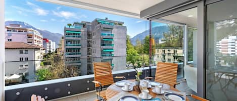 Un balcón con una mesa dispuesta para comer, una silla y vistas a edificios y montañas.