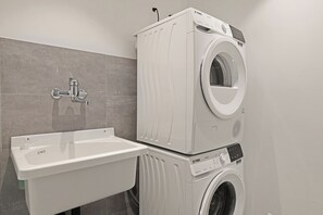 A modern laundry room with a stacked washer and dryer, a white sink, and a grey tiled wall. - Appartamento Lago e Monti - Garage & Terrace in Locarno (Locarno)