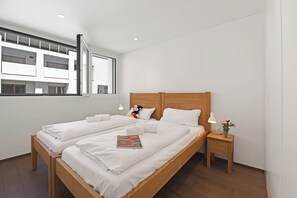 A modern hotel room with a large bed, a nightstand, a window with blinds, and a view of a building outside. - Appartamento Lago e Monti - Garage & Terrace in Locarno (Locarno)