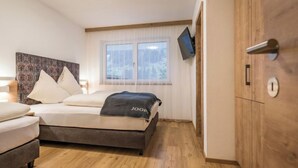 Une chambre moderne avec un lit, un téléviseur fixé au mur et une armoire en bois.