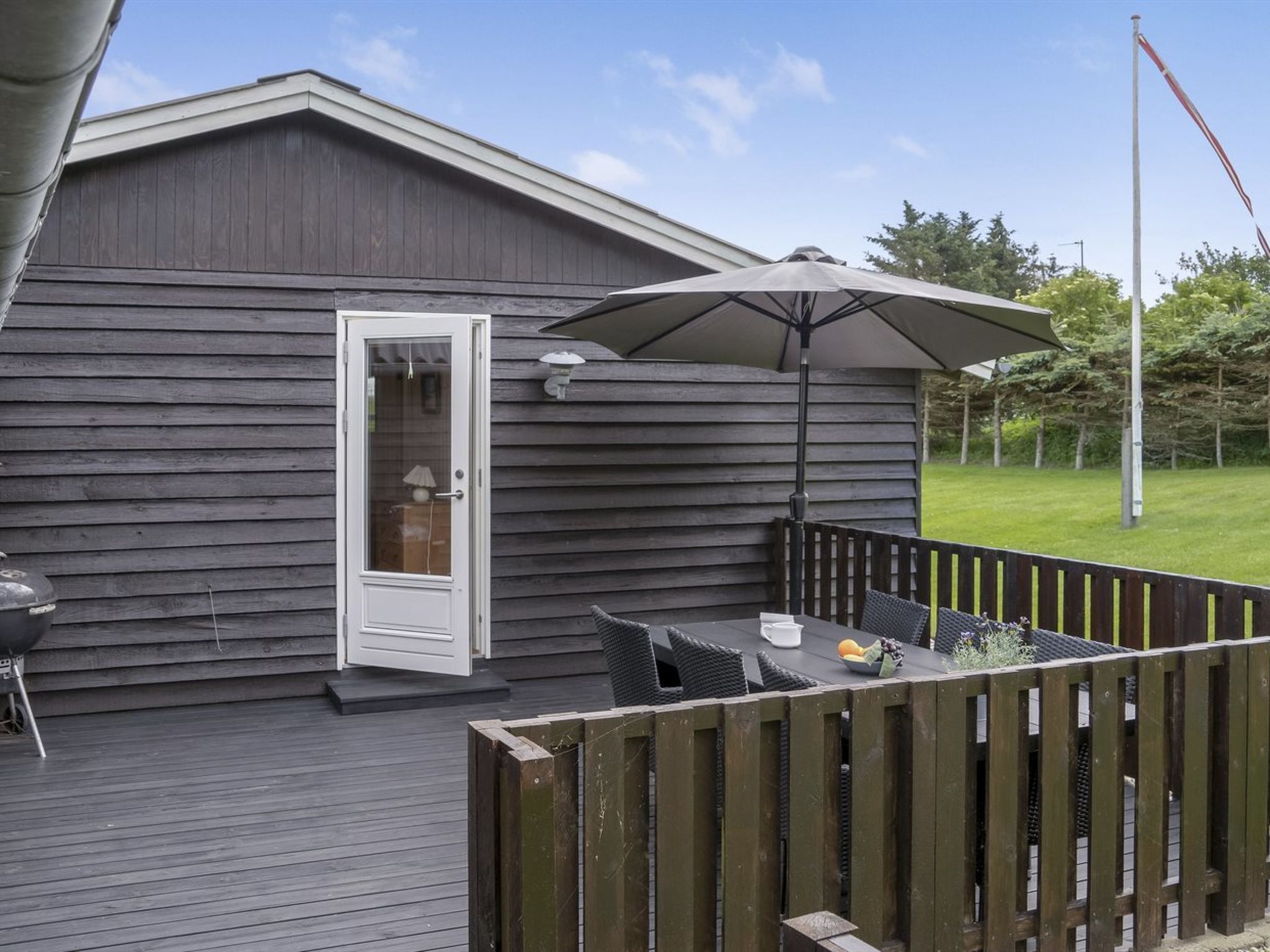 A deck with a table and chairs, a grill, and a door to a building.
