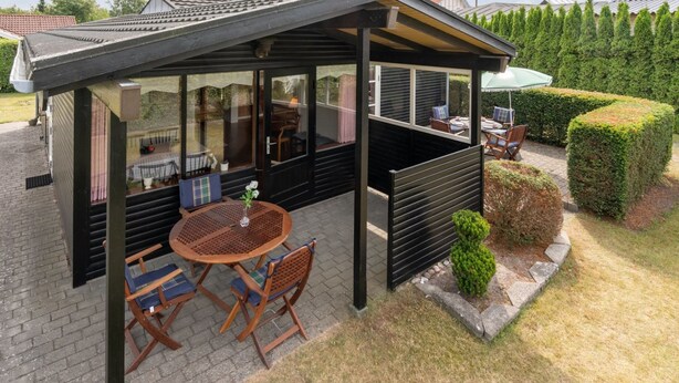 A covered outdoor seating area with a table and chairs, a glass enclosure, and a garden with hedges. - "Siem" - 650m from the sea by Interhome (Væggerløse)
