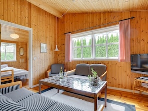 Ein gemütliches Blockhauszimmer mit Holzvertäfelung, einem Essbereich mit Tisch und Stühlen, einem Bett und einem Fernseher.