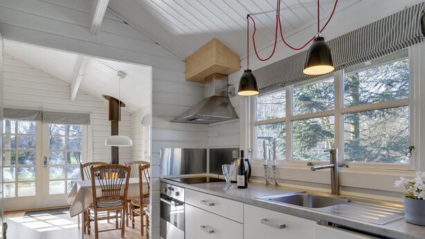 A modern kitchen with white cabinetry, a stainless steel stove, and a large window with a view of trees. - "Freyja" - 800m from the sea by Interhome (Væggerløse)