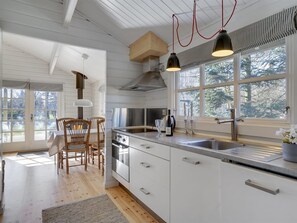 A modern kitchen with white cabinetry, a stainless steel stove, and a large window with a view of trees. - "Freyja" - 800m from the sea by Interhome (Væggerløse)