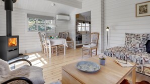 A cozy cabin interior with a wood-burning stove, a dining area with chairs, a kitchen, and a patterned sofa. - "Freyja" - 800m from the sea by Interhome (Væggerløse)