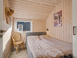 Una habitación pequeña y acogedora con una cama individual, una ventana, una silla y un cuadro colgado en la pared.