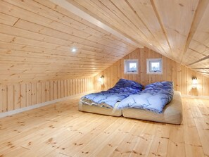 Une chambre mansardée avec de hauts plafonds, des murs et des planchers en bois, un lit superposé et deux petites fenêtres.