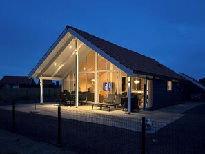 Une maison moderne dotée d’une grande baie vitrée, d’un espace salon extérieur et d’une cour clôturée.