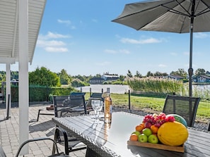 An outdoor patio with a table, chairs, a bottle, and a fruit bowl.
