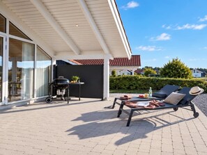 Un espace extérieur abrité comprenant un barbecue, des chaises longues et une table avec de la nourriture et des boissons.