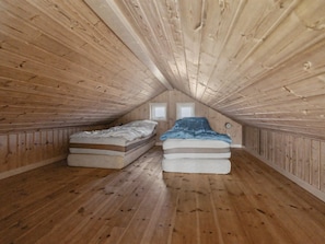 A small attic bedroom with wooden walls and sloped ceilings. There are two beds with mattresses and pillows.