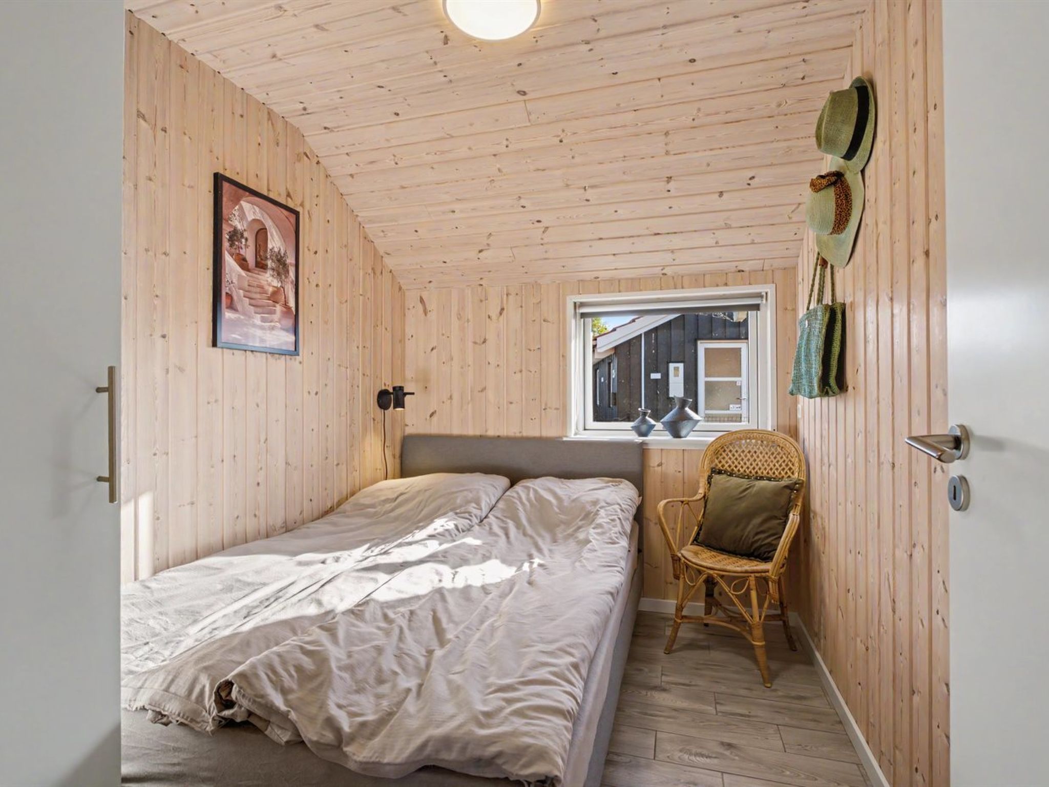 A room with a bed, a chair, a window, and a wall-mounted hat rack.