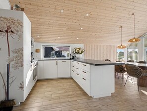 Eine moderne Küche mit weißen Schränken, einer Holzbalkendecke und Blick ins Freie.