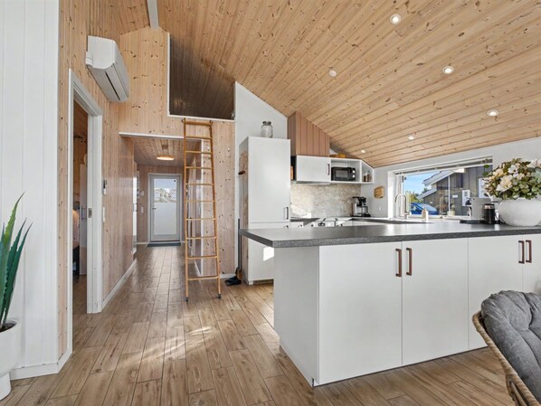 A modern kitchen with a central island, wooden flooring, and a lofted ceiling.