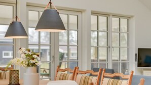 A dining area with a wooden table, striped cushioned chairs, a white vase with flowers, and two black pendant lights. - "Auke" - 100m from the sea by Interhome (Væggerløse)
